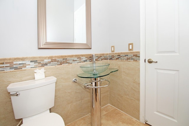 bathroom with tile walls, a wainscoted wall, a sink, and toilet