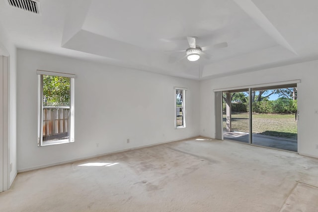 empty room with light colored carpet, visible vents, a healthy amount of sunlight, and a raised ceiling