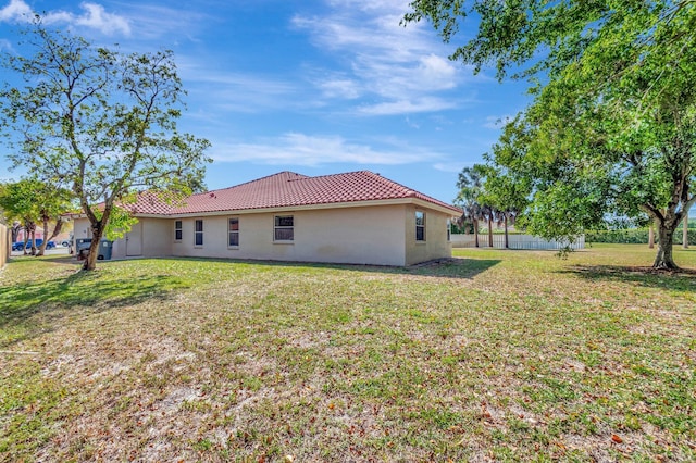 back of house with a lawn, fence, stucco siding, and a tile roof
