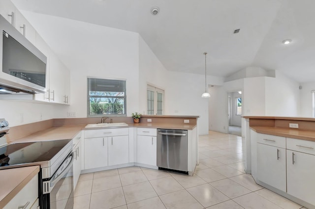 kitchen with light tile patterned flooring, a sink, stainless steel appliances, white cabinetry, and lofted ceiling