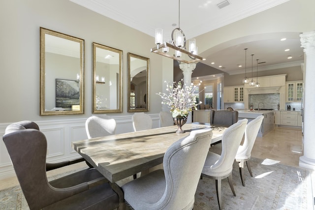 dining space with decorative columns, crown molding, arched walkways, an inviting chandelier, and a decorative wall
