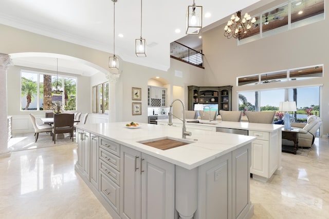 kitchen featuring arched walkways, a sink, a chandelier, ornate columns, and an island with sink