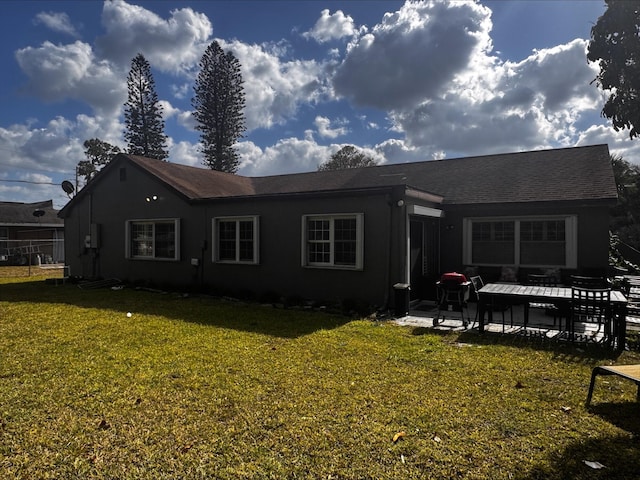 back of house with a lawn, roof with shingles, a patio area, and stucco siding
