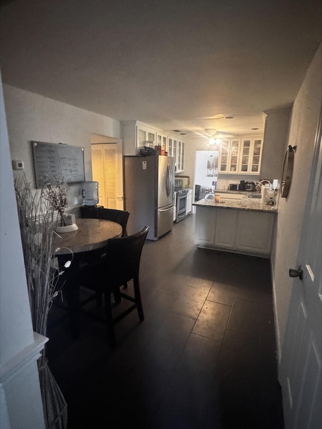 kitchen with white cabinets, glass insert cabinets, a sink, appliances with stainless steel finishes, and a peninsula