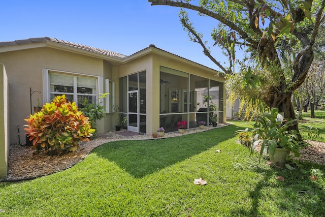 rear view of property with stucco siding, a sunroom, ceiling fan, a lawn, and a tiled roof