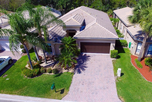 ranch-style house featuring a tiled roof, a front yard, a garage, decorative driveway, and stucco siding