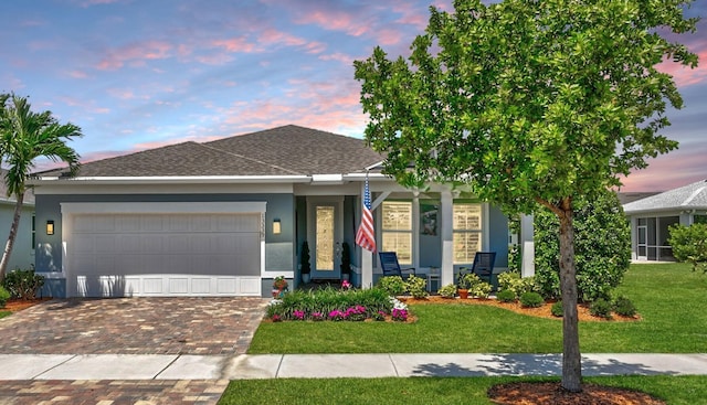 view of front of home featuring decorative driveway, a garage, a shingled roof, and a front lawn