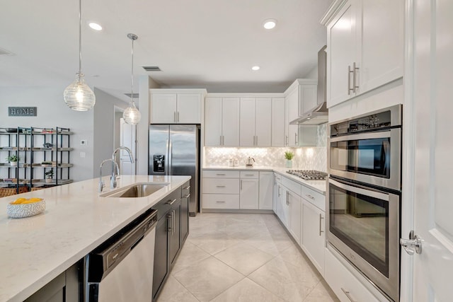 kitchen with visible vents, wall chimney range hood, tasteful backsplash, a sink, and appliances with stainless steel finishes