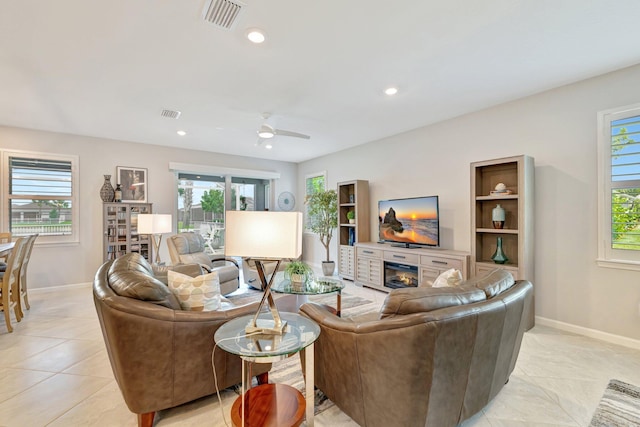 living area with a glass covered fireplace, baseboards, a ceiling fan, and visible vents