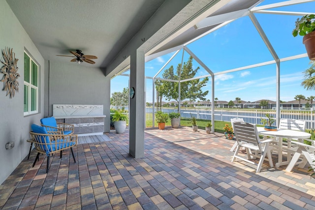 view of patio / terrace featuring glass enclosure, a water view, fence, and a ceiling fan