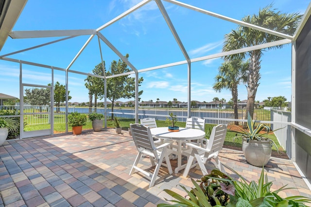 view of patio featuring fence, outdoor dining area, glass enclosure, and a water view