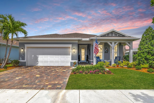 view of front facade featuring a porch, decorative driveway, a front lawn, an attached garage, and stucco siding