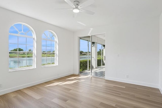 unfurnished room featuring wood finished floors, ceiling fan, baseboards, and a water view