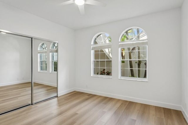 unfurnished bedroom with multiple windows, light wood finished floors, baseboards, and a closet