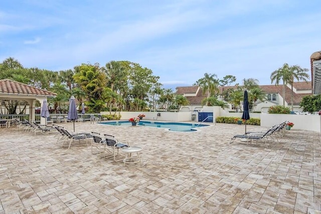 community pool with fence, a gazebo, and a patio