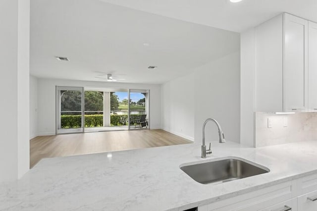 kitchen with a sink, light stone counters, white cabinetry, light wood-style floors, and open floor plan