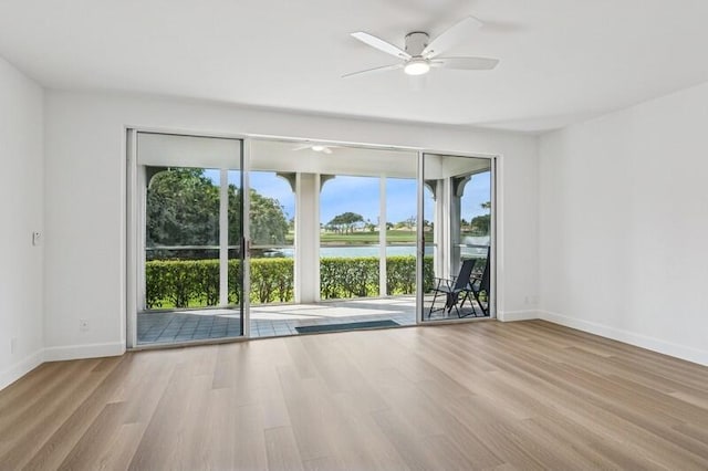empty room with a ceiling fan, baseboards, wood finished floors, and a water view