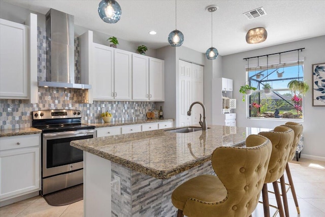 kitchen with electric range, wall chimney exhaust hood, a sink, light tile patterned floors, and backsplash