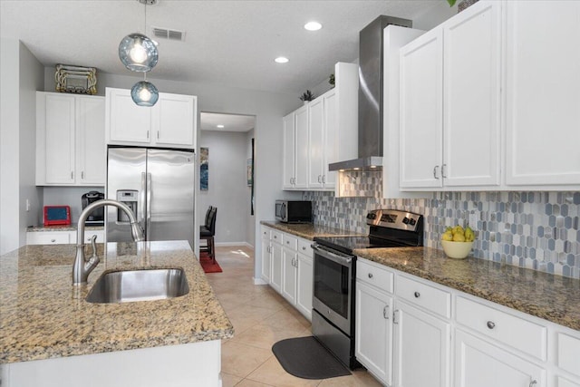 kitchen featuring appliances with stainless steel finishes, a sink, backsplash, wall chimney range hood, and white cabinetry
