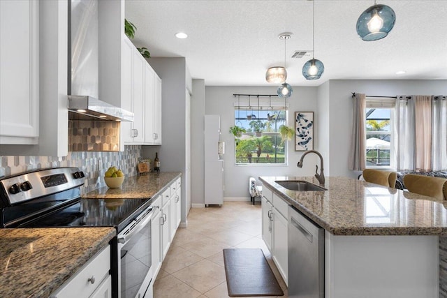 11400 SW Reston Ct, Port Saint Lucie, FL 34987 - kitchen with stainless steel appliances, wall chimney exhaust hood, tasteful backsplash, a kitchen island with sink, and white cabinets