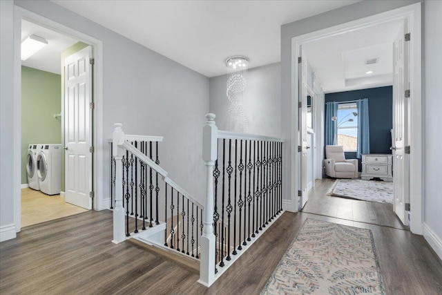 hallway with an upstairs landing, washing machine and clothes dryer, wood finished floors, and baseboards