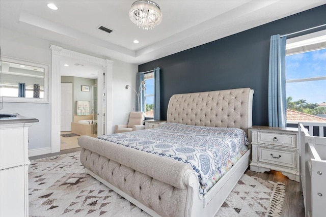 bedroom featuring light wood-style flooring, a chandelier, ensuite bathroom, a tray ceiling, and recessed lighting
