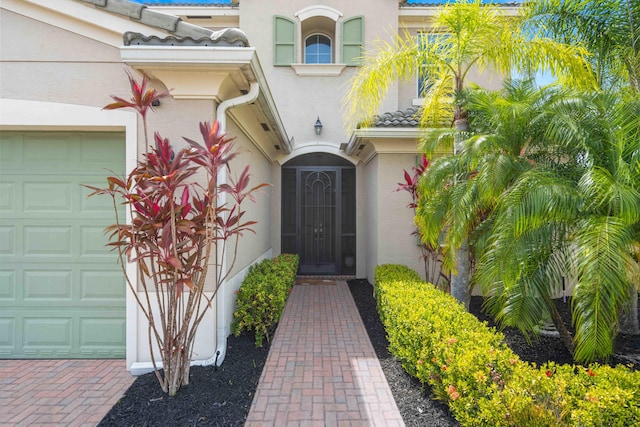 doorway to property with an attached garage, stucco siding, and a tiled roof