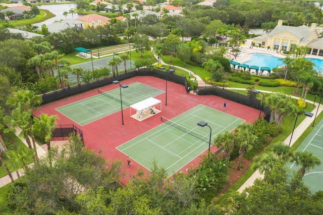 view of tennis court featuring fence, a community pool, and a water view