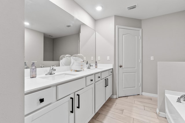 885 SW Squirrel Ave, Port Saint Lucie, FL 34953 - bathroom featuring a garden tub, double vanity, wood finish floors, baseboards, and recessed lighting