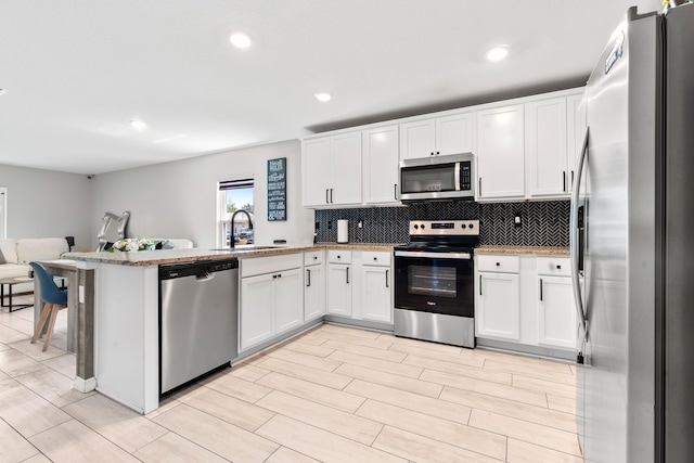 885 SW Squirrel Ave, Port Saint Lucie, FL 34953 - kitchen with stainless steel appliances, a sink, a peninsula, open floor plan, and white cabinetry