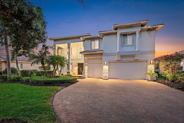 view of front of property featuring a tiled roof, a garage, a yard, stucco siding, and decorative driveway