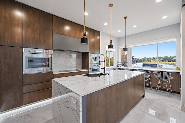 kitchen featuring light stone counters, black electric stovetop, recessed lighting, an island with sink, and marble finish floor