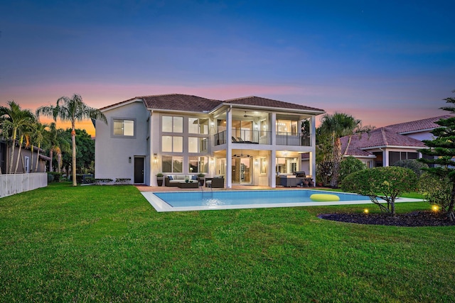 rear view of property featuring ceiling fan, a balcony, a yard, stucco siding, and an outdoor living space