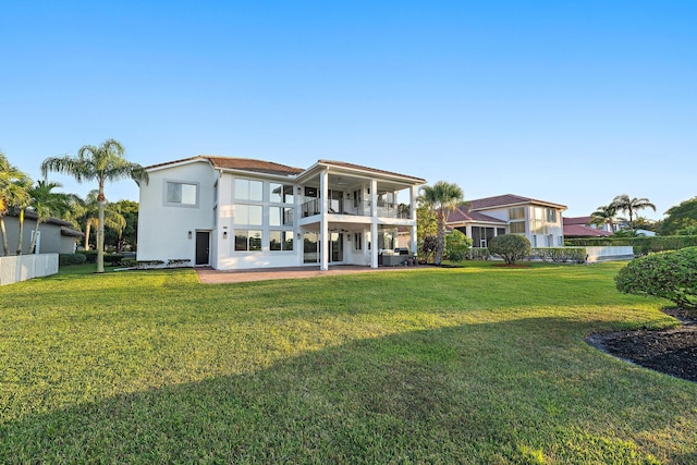 rear view of property featuring stucco siding, a patio area, a balcony, and a lawn