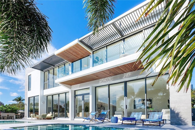 back of property featuring stucco siding, a balcony, a community pool, and a patio