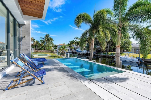 outdoor pool with fence, a water view, and a patio