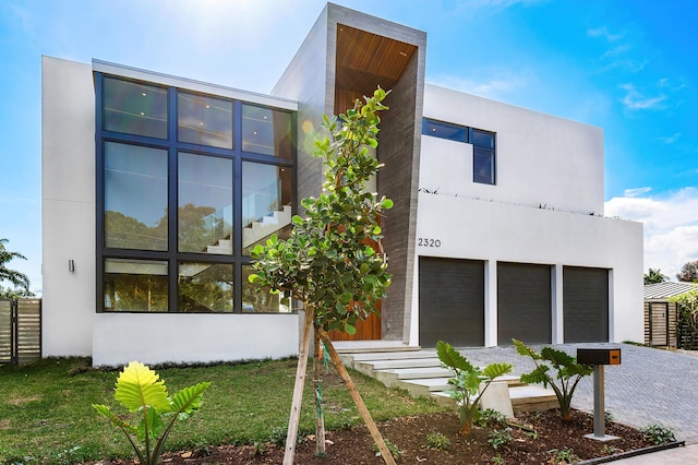 exterior space featuring an attached garage, stucco siding, fence, and decorative driveway