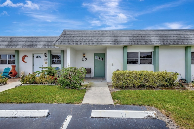 front of property with a shingled roof, a front lawn, stucco siding, and mansard roof