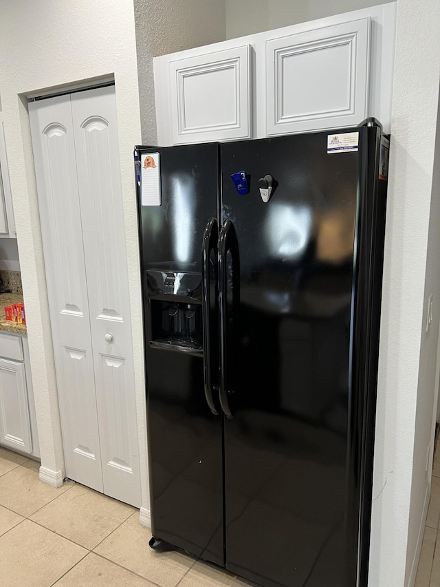 kitchen with black fridge with ice dispenser, light tile patterned flooring, light stone counters, and white cabinetry
