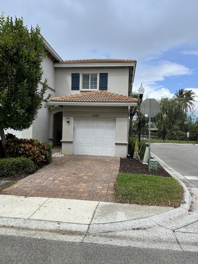 view of front of house featuring an attached garage, a tile roof, decorative driveway, and stucco siding