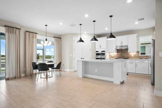 kitchen featuring visible vents, under cabinet range hood, light countertops, appliances with stainless steel finishes, and decorative backsplash