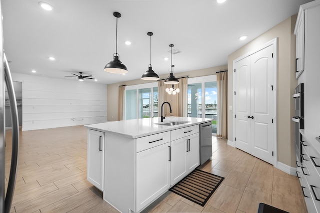 kitchen featuring stainless steel dishwasher, ceiling fan, a sink, light countertops, and an island with sink