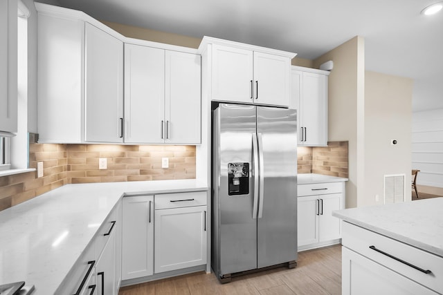 kitchen featuring light stone counters, visible vents, backsplash, stainless steel fridge, and white cabinets