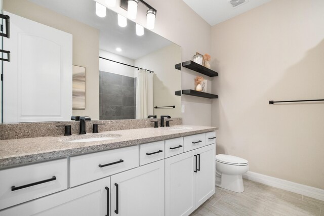 full bath featuring toilet, baseboards, double vanity, and a sink