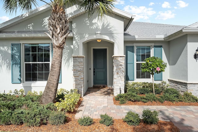 property entrance with stone siding, a shingled roof, and stucco siding