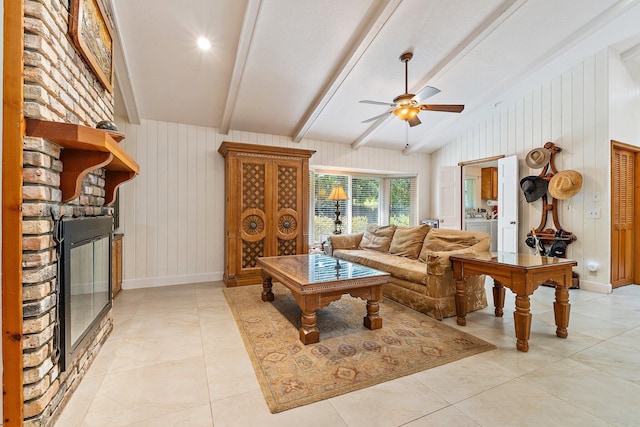 living room featuring a ceiling fan, a fireplace, baseboards, vaulted ceiling with beams, and light tile patterned flooring