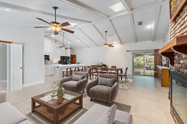 living area with light tile patterned floors, a ceiling fan, lofted ceiling with skylight, and visible vents