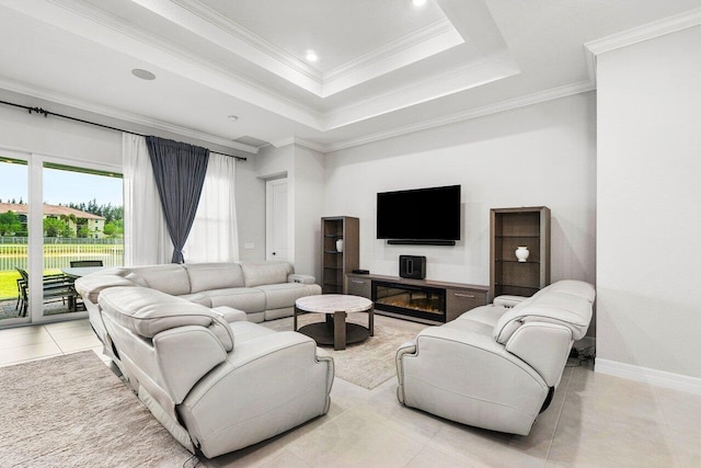 living area with crown molding, a glass covered fireplace, a tray ceiling, recessed lighting, and light tile patterned flooring