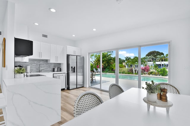 kitchen featuring white cabinets, light stone counters, light wood-style floors, stainless steel appliances, and tasteful backsplash