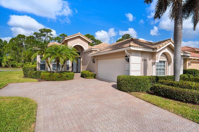 mediterranean / spanish-style house featuring stucco siding, decorative driveway, a tiled roof, and an attached garage